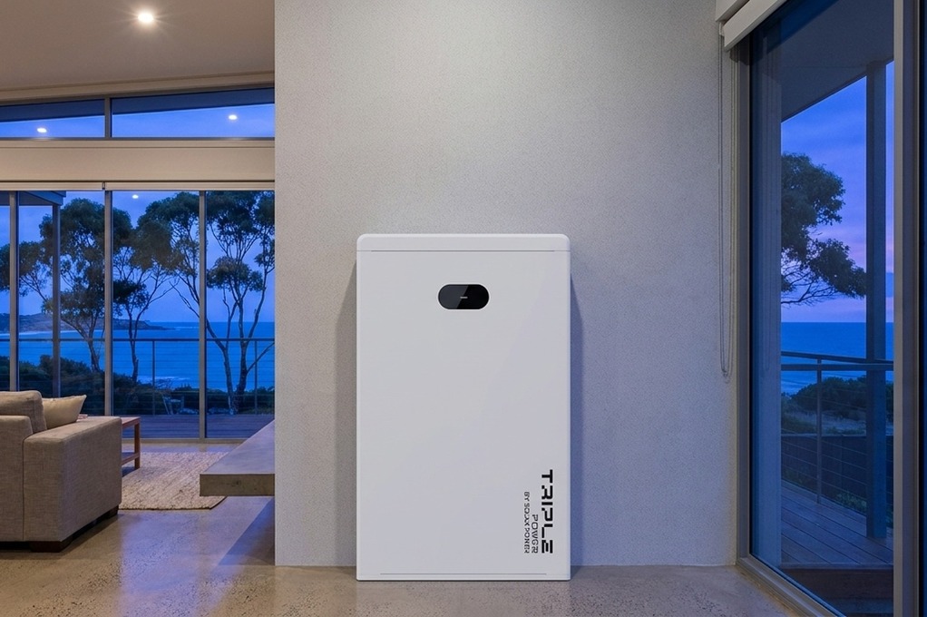 Triple Power battery by SolaX Power against a grey wall between two floor-to-ceiling windows, coastal dusk lighting.