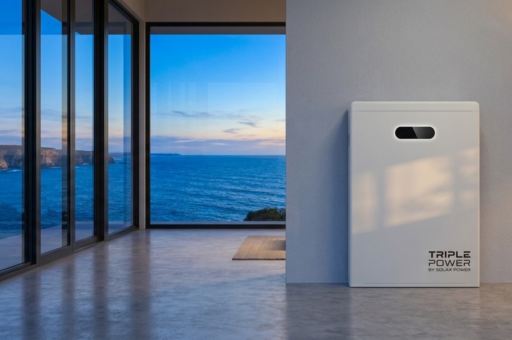 Triple Power by SolaX Power battery unit against a grey wall with floor-to-ceiling windows overlooking a rocky coastline at dusk.