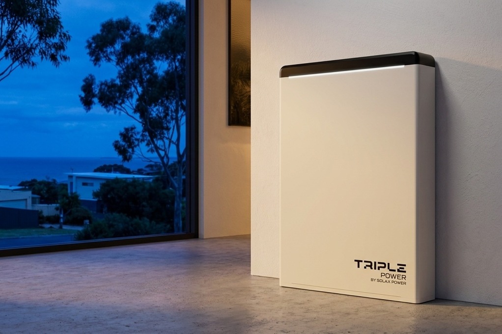 Triple Power battery by SolaX Power against a white wall in an interior room at dusk, gum trees and ocean visible through window.