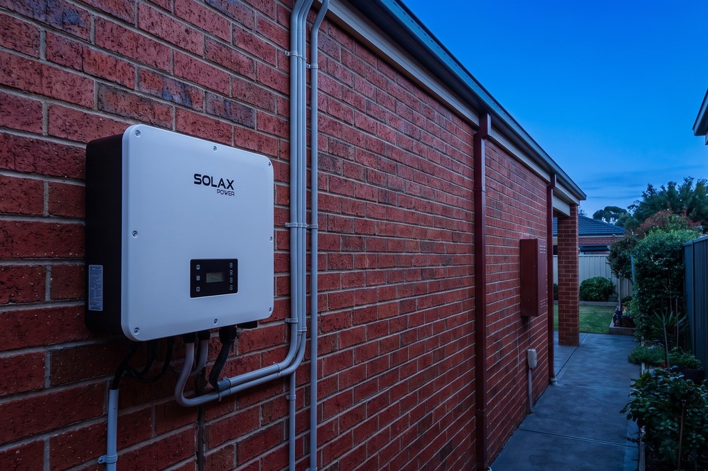SolaX inverter mounted on a brick exterior wall at dusk
