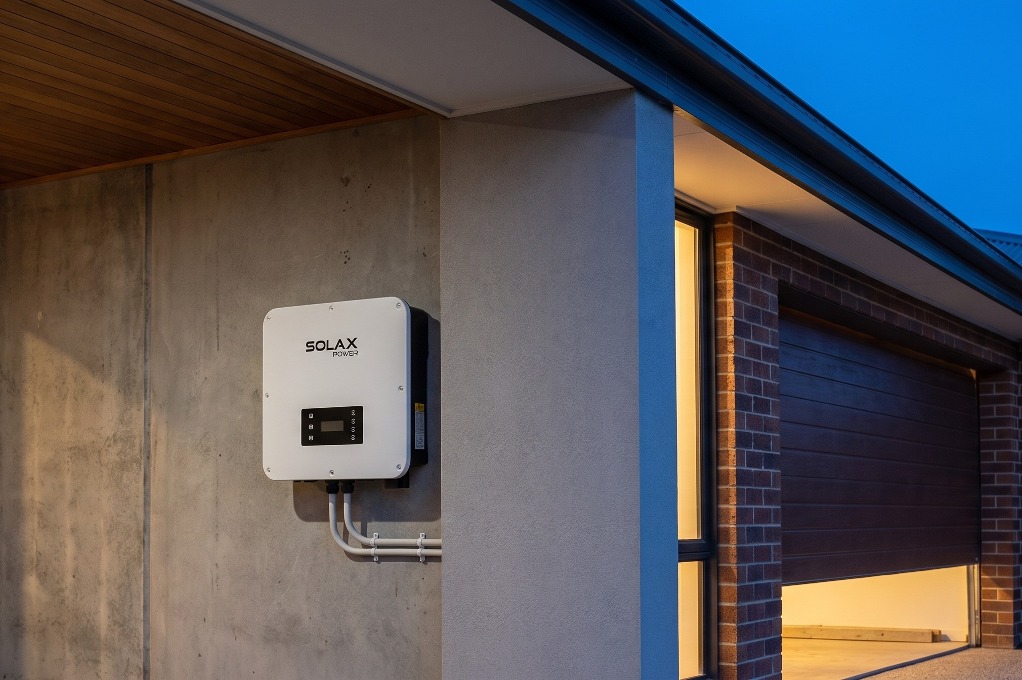 SolaX hybrid inverter mounted on an exterior wall at dusk, with an open garage door in the background
