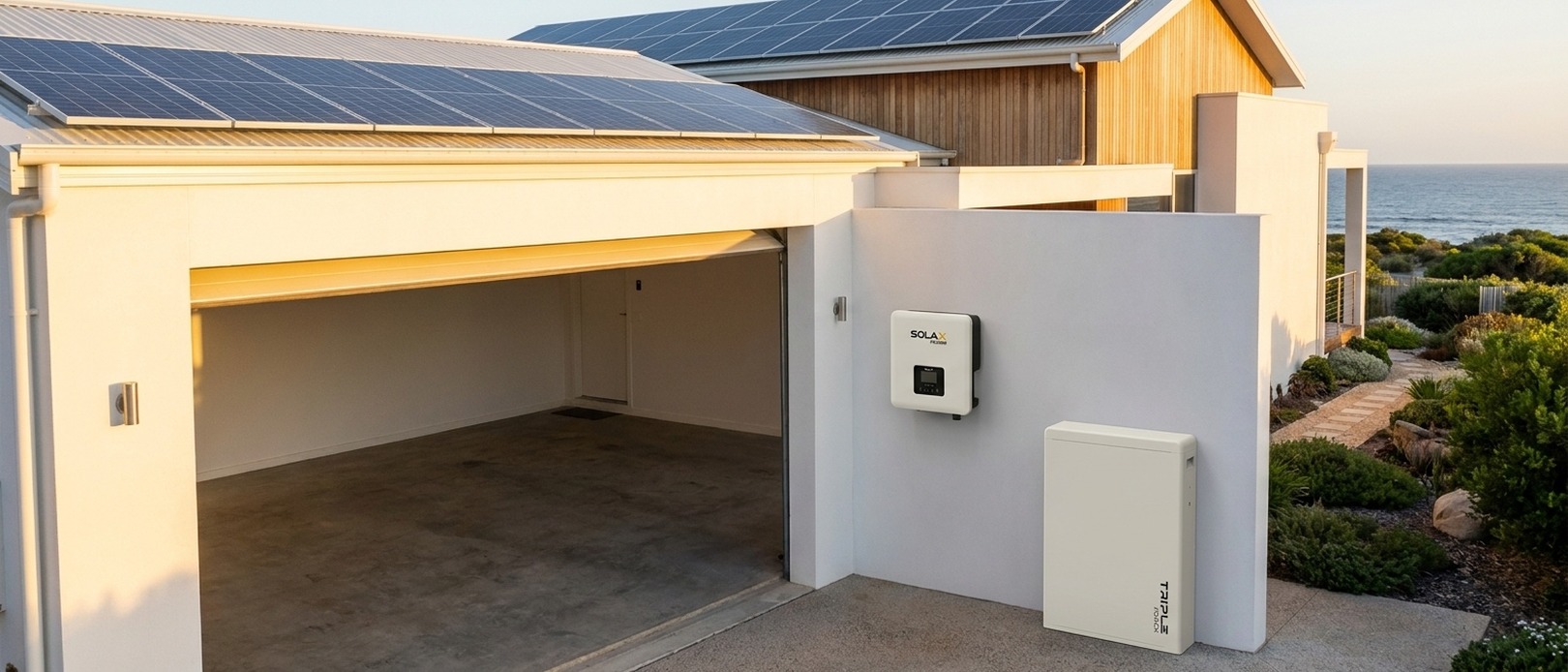 SolaX Power inverter and Triple Power battery mounted on the exterior white render wall of a coastal home at golden hour, solar panels visible on roof.