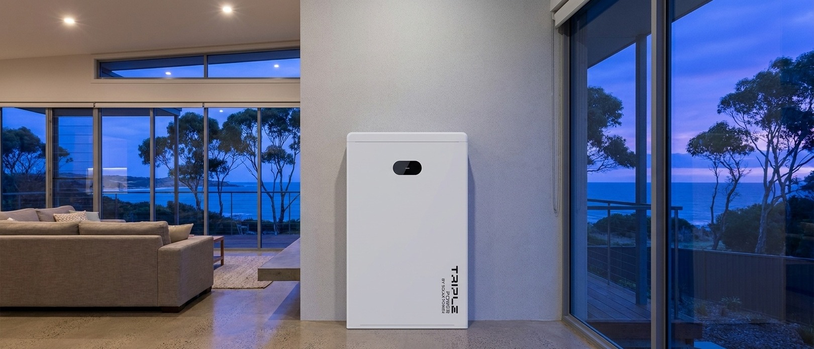 Triple Power battery by SolaX Power leaning against an interior wall at dusk, modern coastal living room and ocean views on either side.