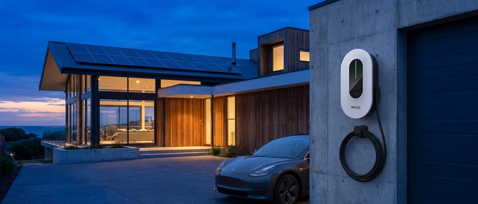SolaX EV Charger mounted on a concrete garage wall at dusk, with a Tesla Model 3 in the driveway and a solar-panelled home in the background.