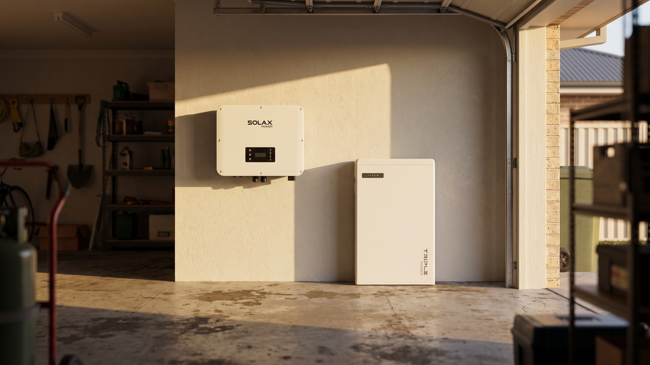 SolaX hybrid inverter mounted on the wall of an Australian garage next to a SolaX Triple Power battery on the floor, in warm afternoon light